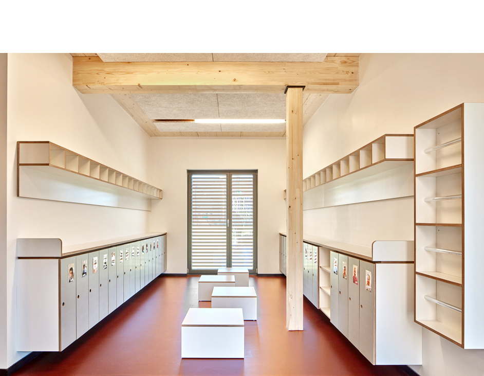 Aloys Kiefer Architekturfotografie: Querformatige Innenaufnahme von einem Garderobenraum für Kinder. Weißes Dekor der Schränke und Ablagefächer. Auf der rechten Bildhälfte ein Holzständer der einen Deckenbalken stützt.