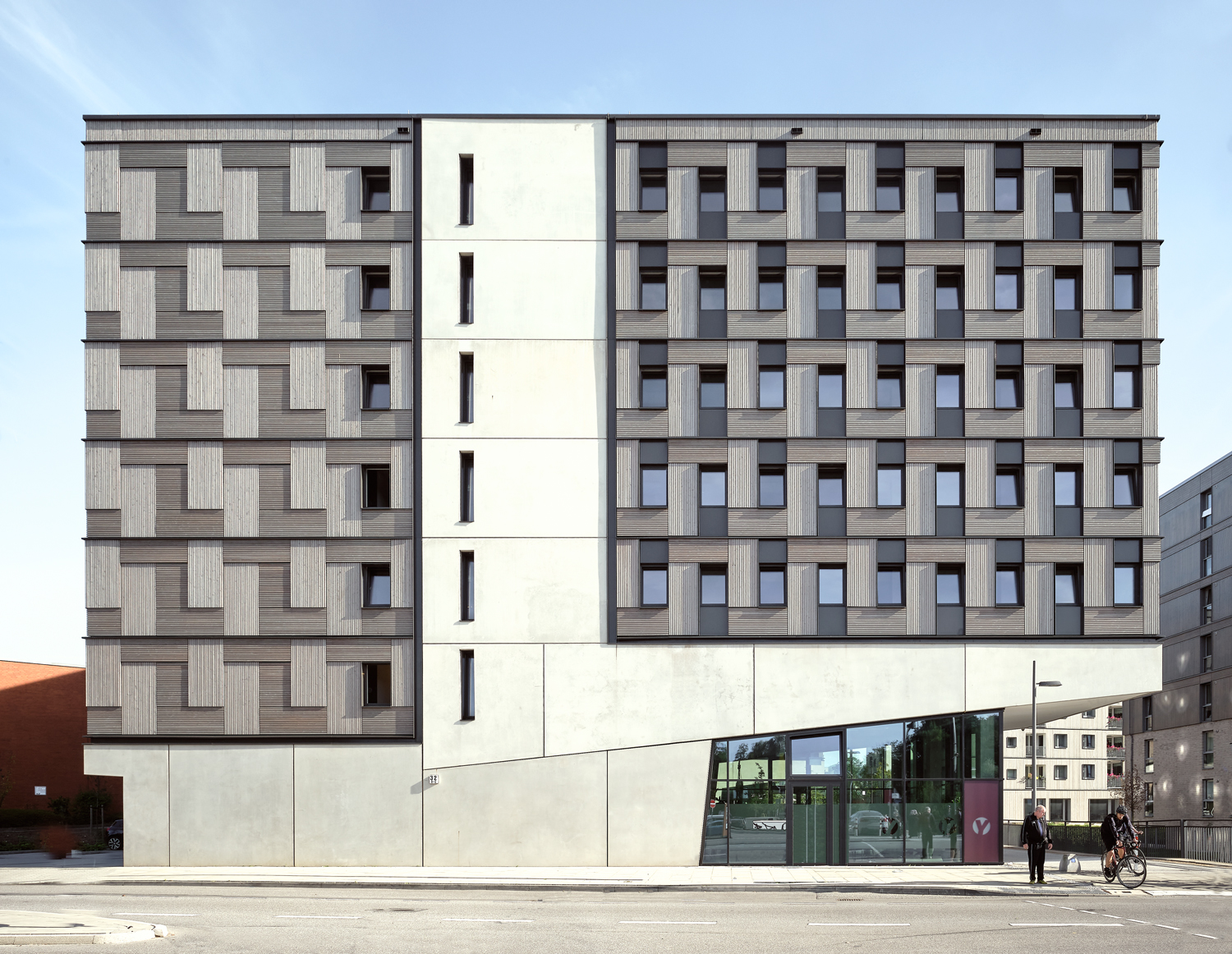 Aloys Kiefer Architekturfotografie: Querformat der ganzen Fassade von Sonne beschienen. Die Fassade weist drei Elemente auf. Den Betonsockel mit der keilförmig auskragendem Stütze nach rechts.